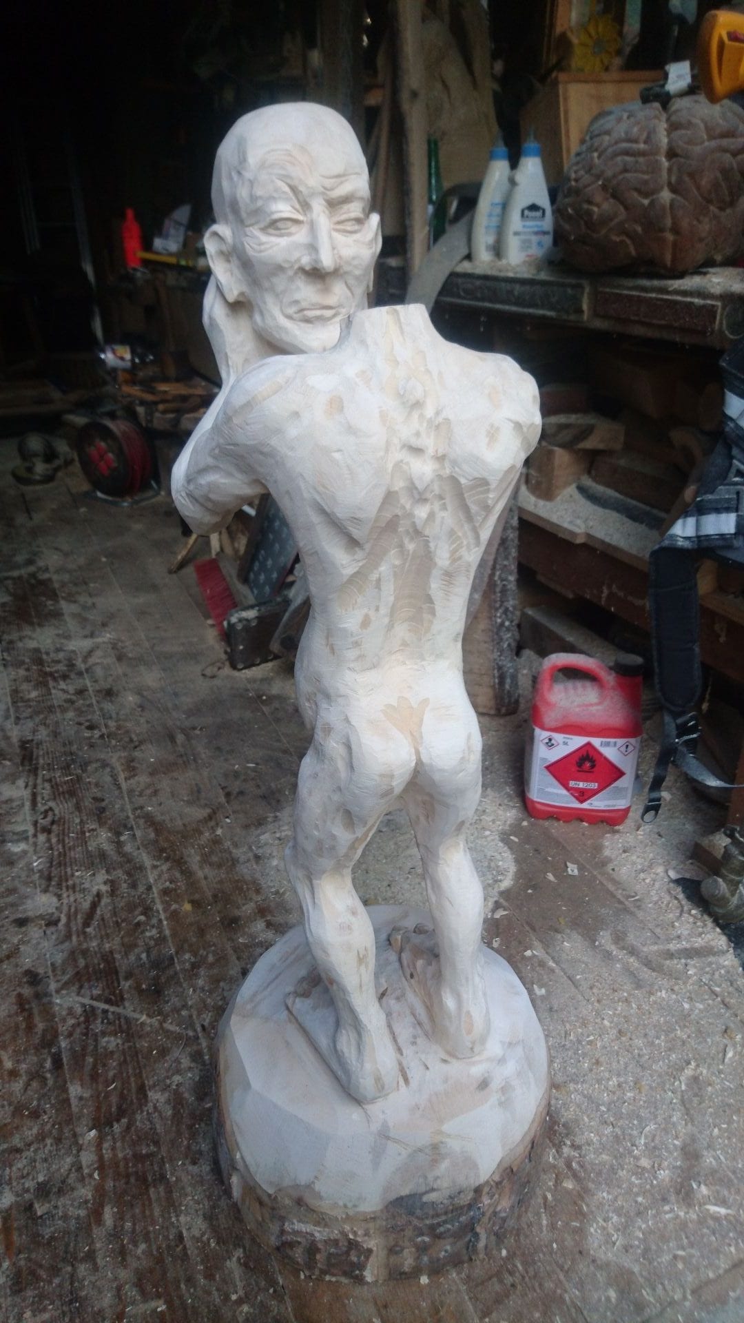 Geschnitzte Figur aus Ahornholz | ein Menschenwesen welches seinen eigenen Kopf trägt und vor sich mit ausgestreckten Armen hält.