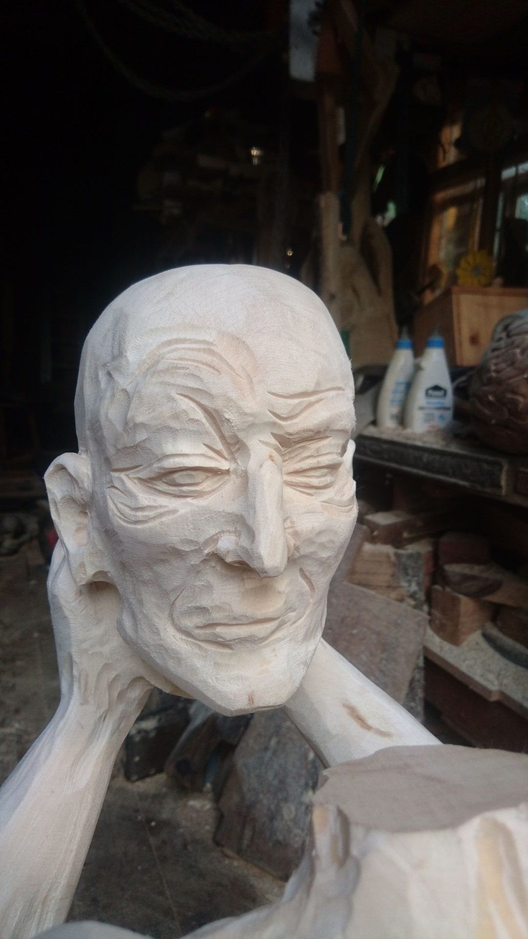 Geschnitzte Figur aus Ahornholz | ein Menschenwesen welches seinen eigenen Kopf trägt und vor sich mit ausgestreckten Armen hält. Mit sicht zum Gesicht.