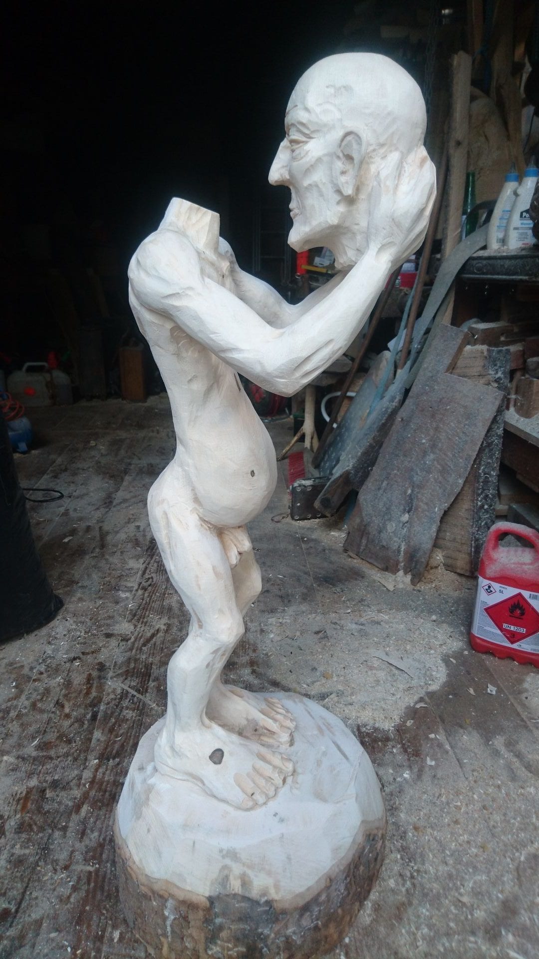 Geschnitzte Figur aus Ahornholz | ein Menschenwesen welches seinen eigenen Kopf trägt und vor sich mit ausgestreckten Armen hält. Mit sicht zur rechten Seite.