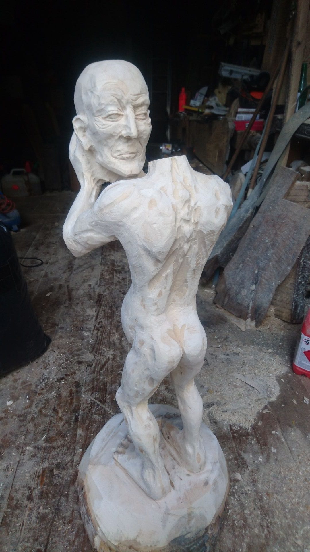 Geschnitzte Figur aus Ahornholz | ein Menschenwesen welches seinen eigenen Kopf trägt und vor sich mit ausgestreckten Armen hält. Mit sicht von hinten.