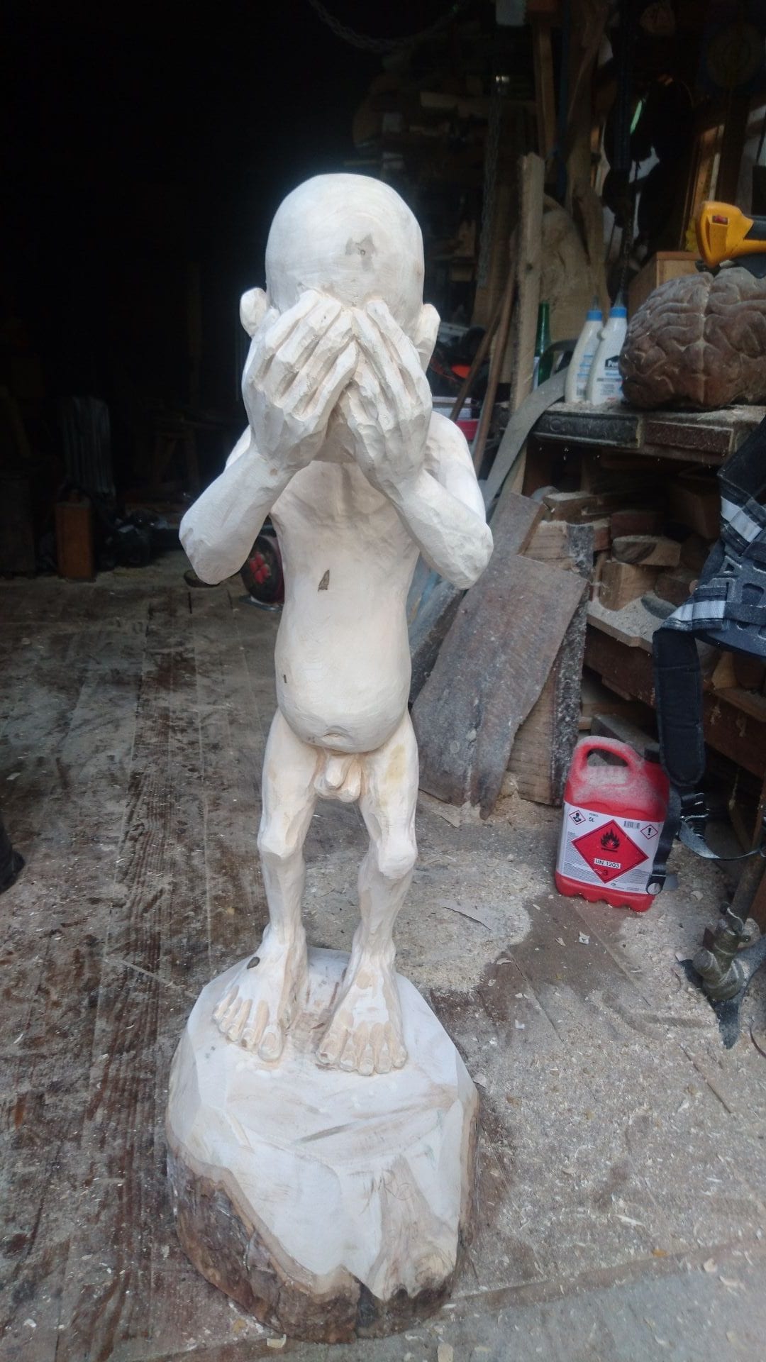 Geschnitzte Figur aus Ahornholz | ein Menschenwesen welches seinen eigenen Kopf trägt und vor sich mit ausgestreckten Armen hält. Mit sicht von Vorne.