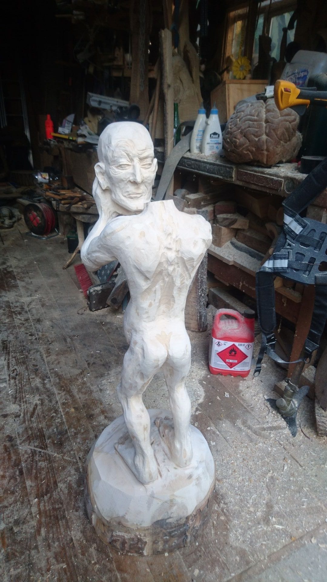 Geschnitzte Figur aus Ahornholz | ein Menschenwesen welches seinen eigenen Kopf trägt und vor sich mit ausgestreckten Armen hält. Mit sicht von hinten.