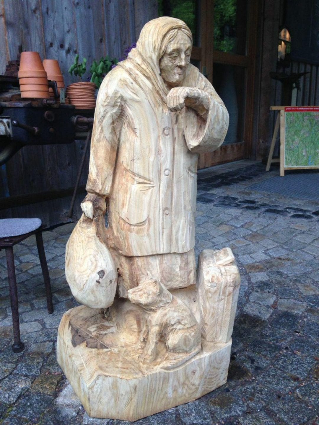 Geschnitzte Figur aus Holz | eine Oma die auf Ihr linkes Handgelenk schaut und im der rechten Hand einen Sack hält. Vor Ihr sitzt ein kleiner Hund.